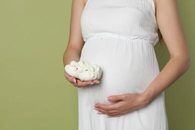 Photo of Young pregnant woman with pair of baby shoes on light olive background, closeup