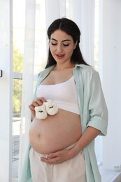 Photo of Portrait of beautiful pregnant woman with baby shoes at home