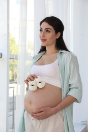 Portrait of beautiful pregnant woman with baby shoes at home