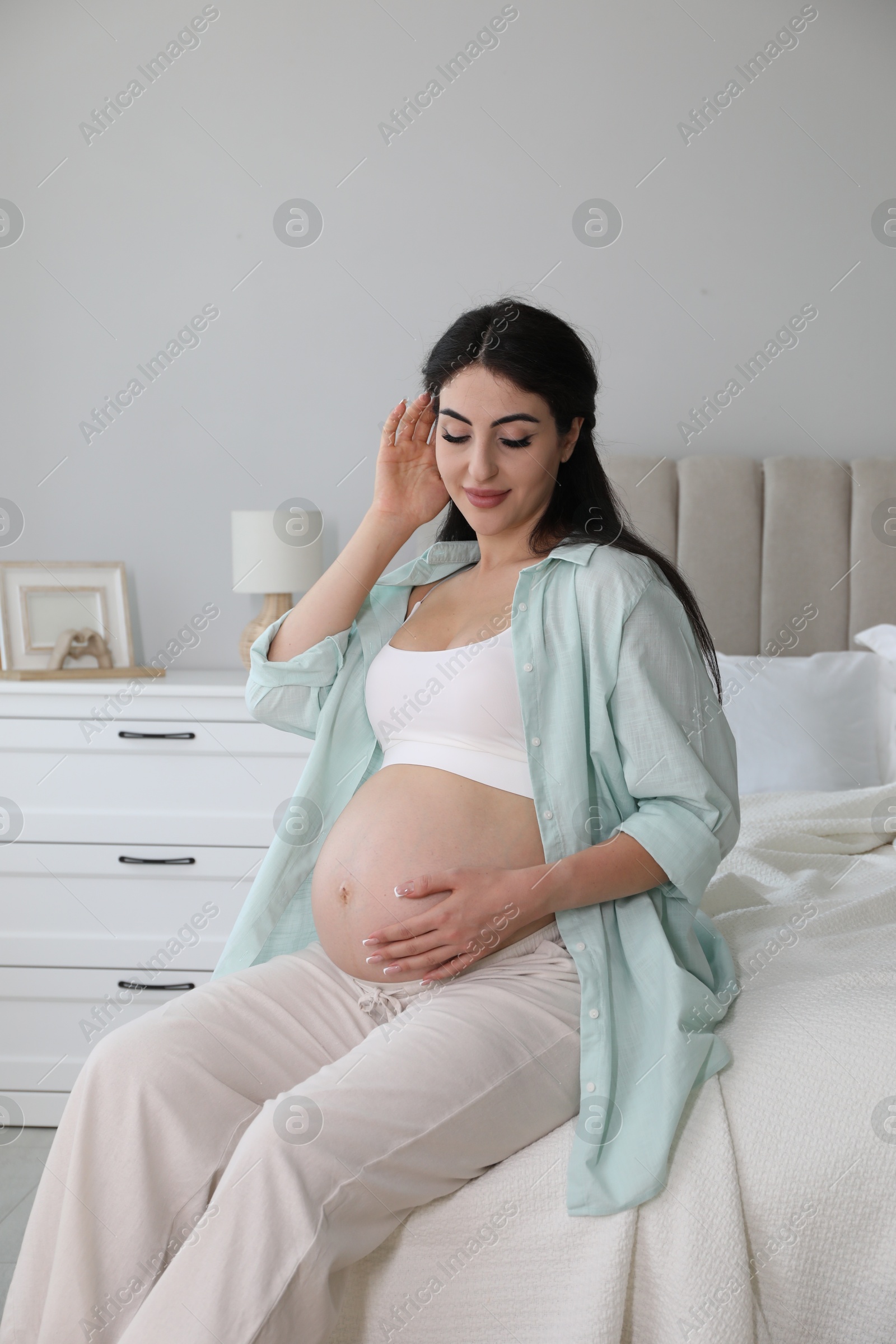 Photo of Young pregnant woman sitting on bed at home