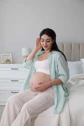 Photo of Young pregnant woman sitting on bed at home