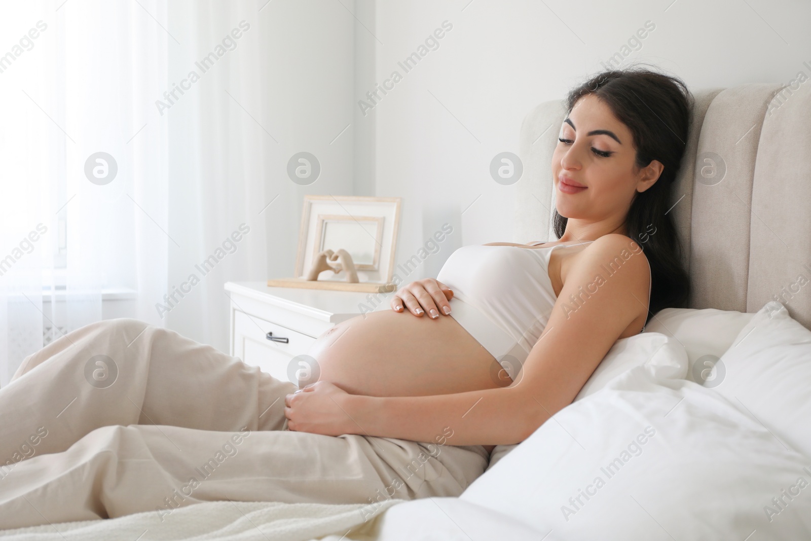 Photo of Young pregnant woman lying on bed at home