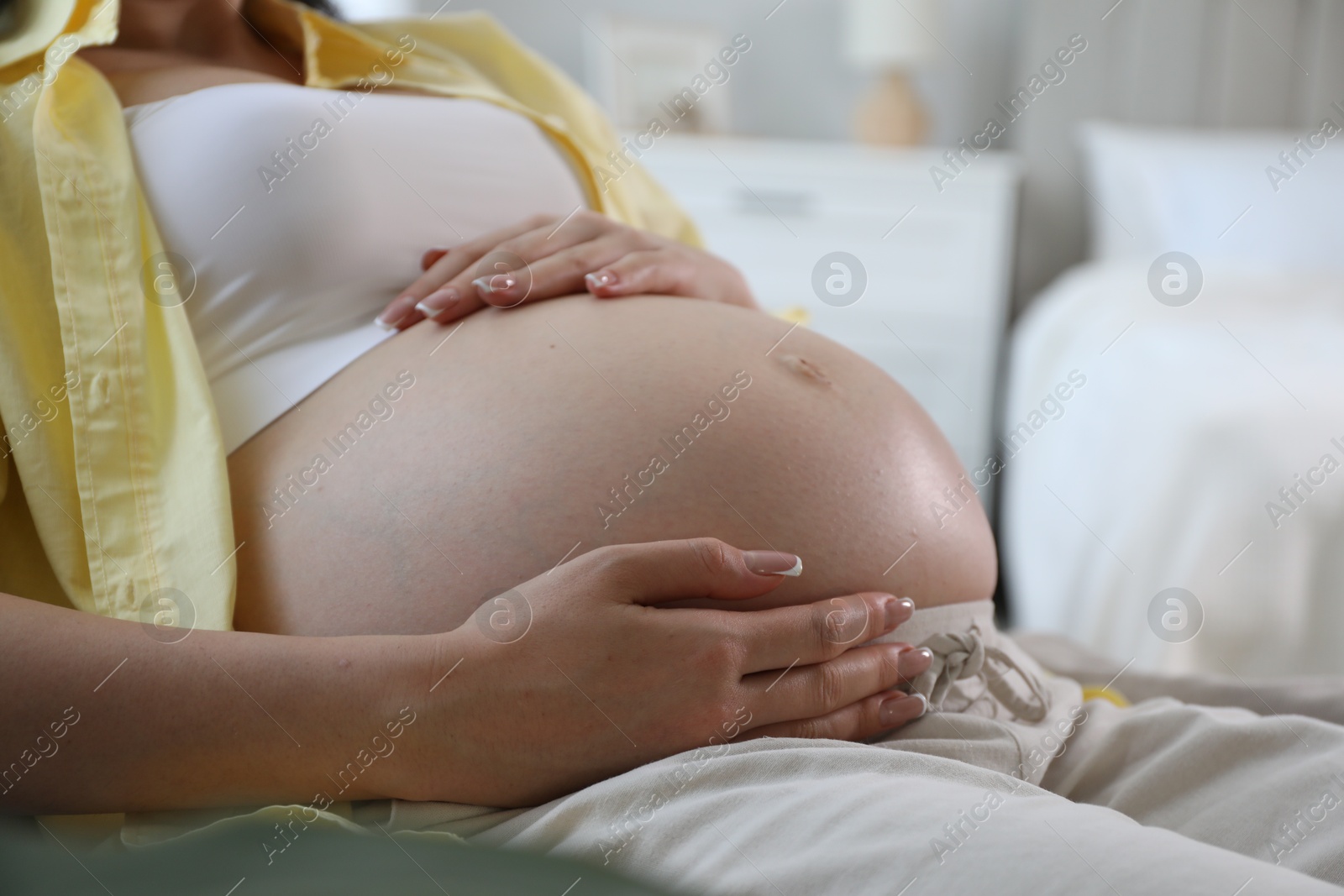 Photo of Young pregnant woman lying on bed at home, closeup