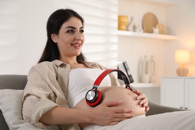 Young pregnant woman with headphones on belly at home