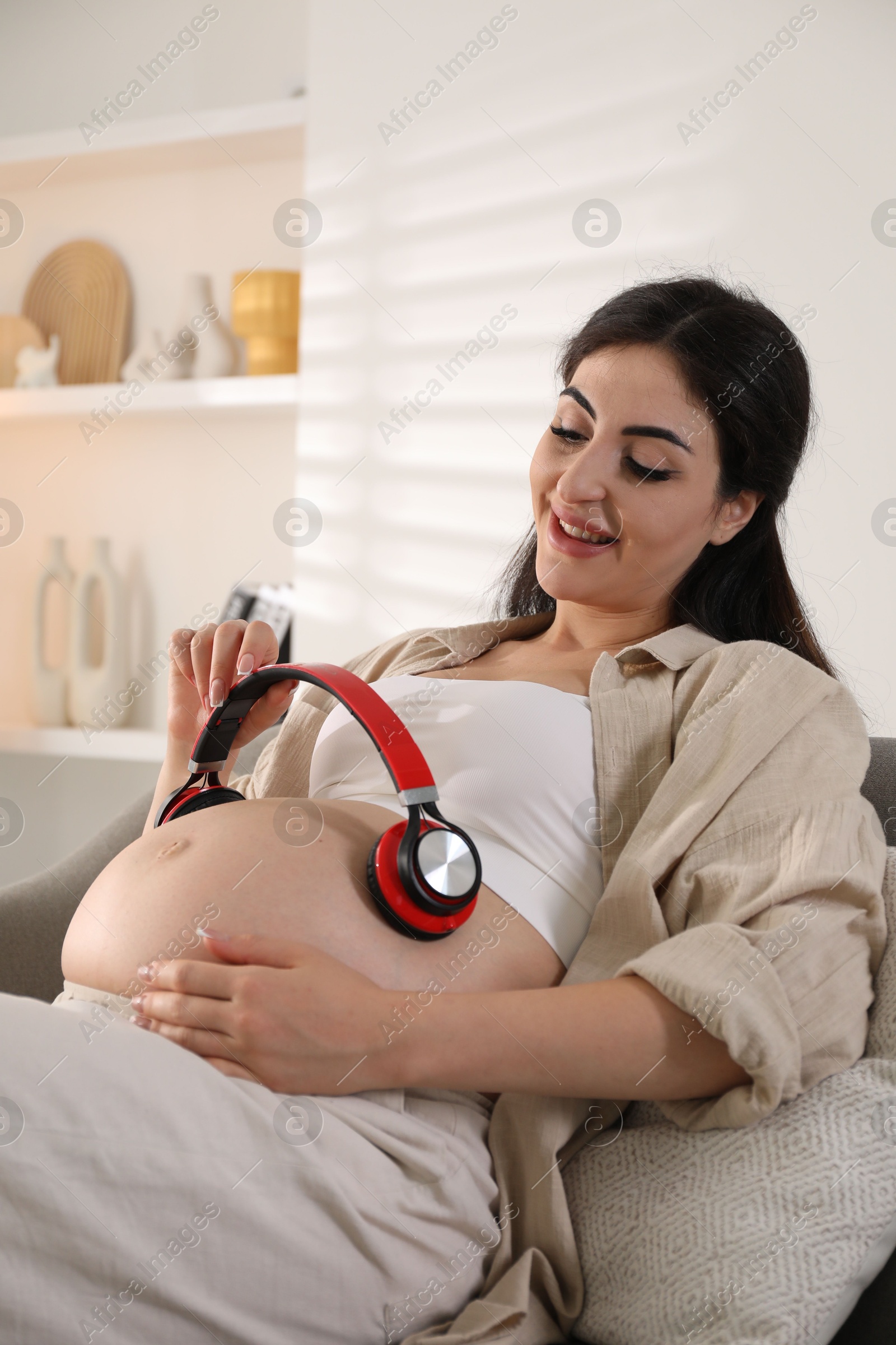 Photo of Young pregnant woman with headphones on belly at home