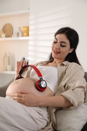 Young pregnant woman with headphones on belly at home