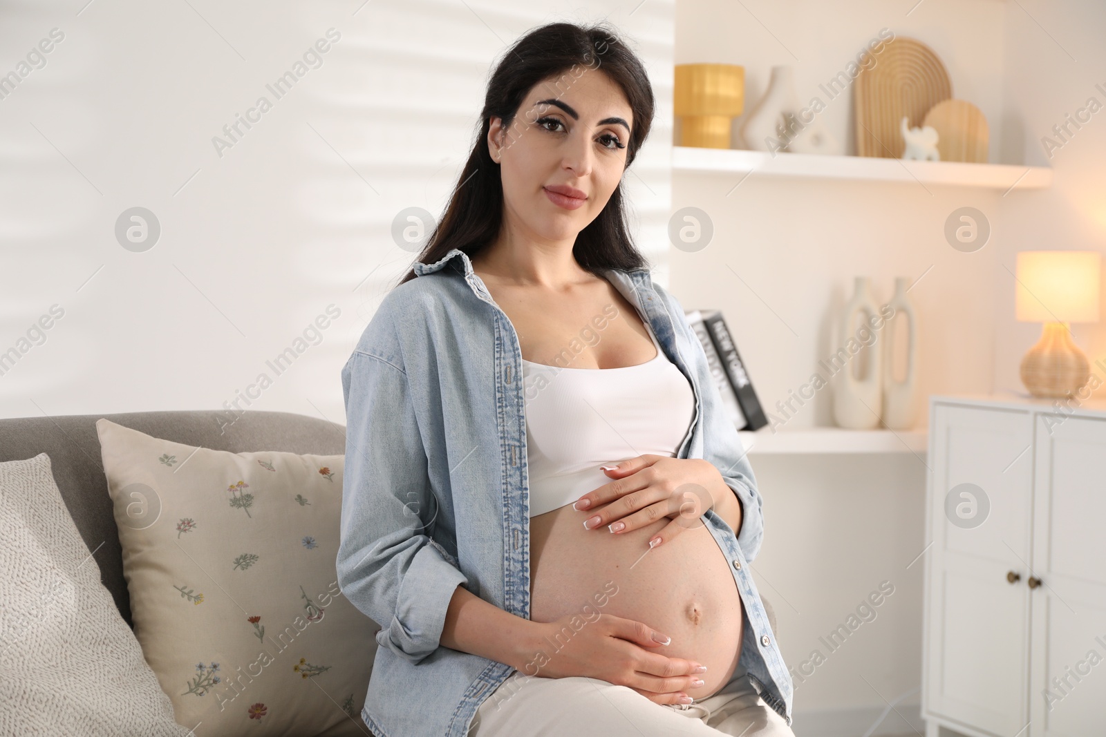 Photo of Young pregnant woman sitting on sofa at home