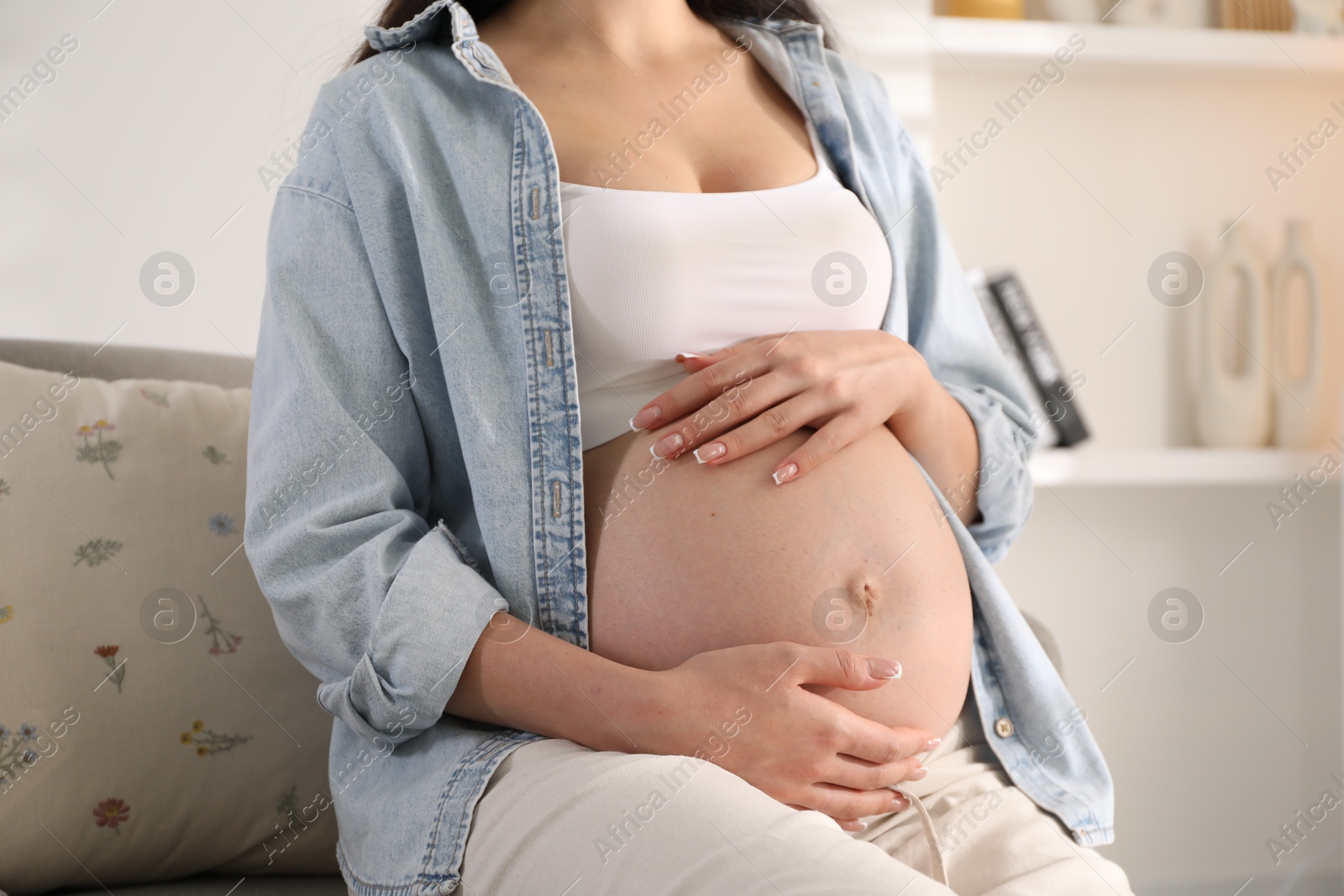 Photo of Young pregnant woman sitting on sofa at home, closeup