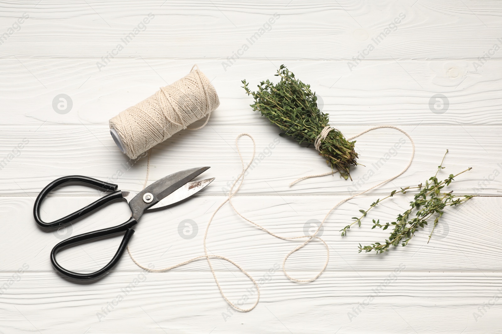 Photo of Fresh herb. Bunch of thyme, spool of thread and scissors on white wooden table, flat lay