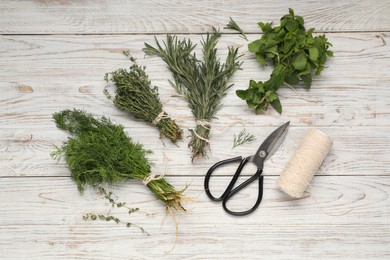 Photo of Bunches of different fresh herbs, spool of thread and scissors on white wooden table, flat lay