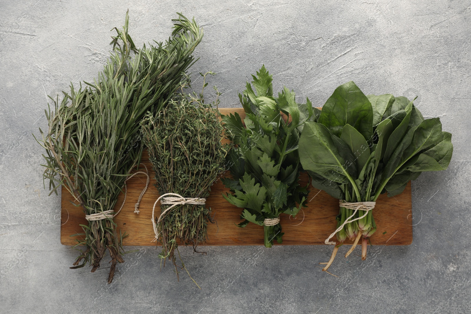 Photo of Bunches of different fresh herbs on grey textured table, flat lay