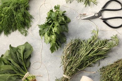 Photo of Bunches of different fresh herbs, thread and scissors on light grey textured table, flat lay