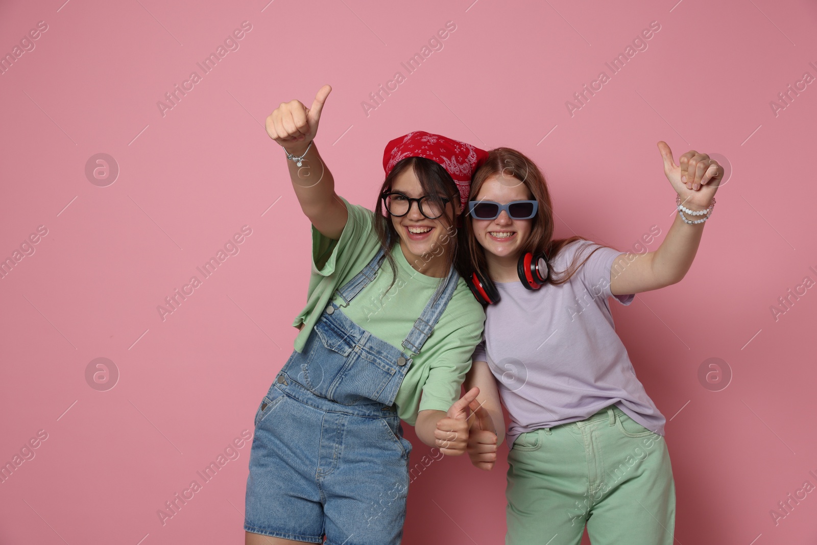 Photo of Happy teenage girls showing thumbs up on pink background