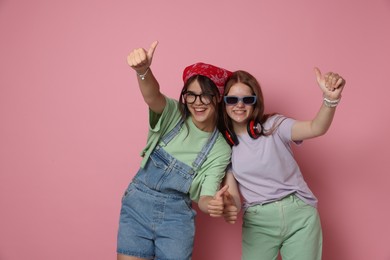 Happy teenage girls showing thumbs up on pink background