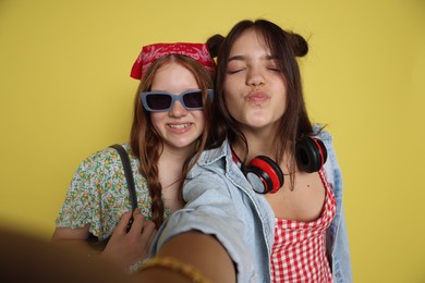 Happy teenage girls taking selfie on yellow background