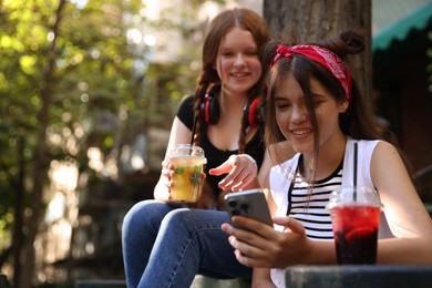 Happy teenage friends looking at smartphone in outdoor cafe. Space for text