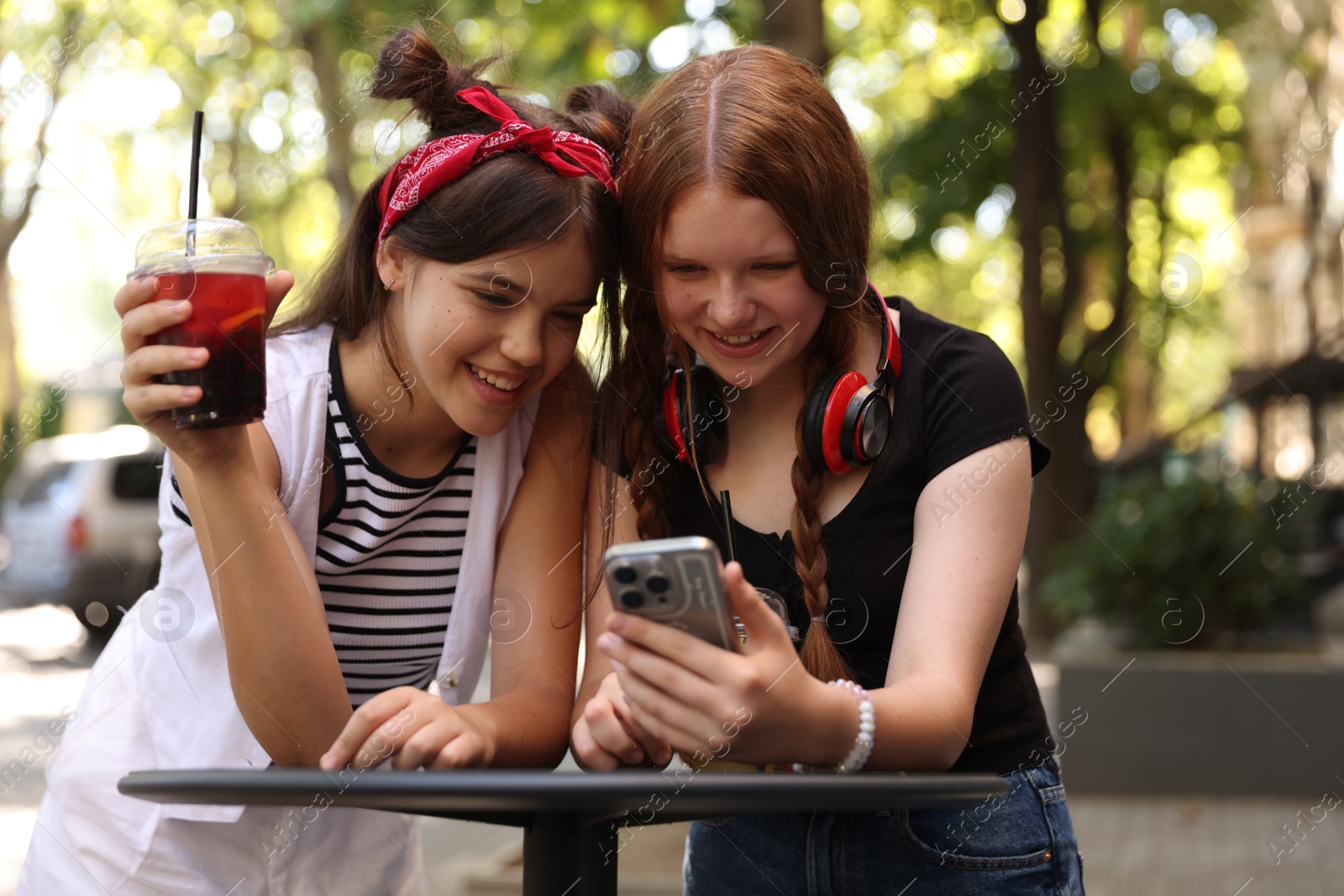 Photo of Happy teenage friends looking at smartphone in outdoor cafe