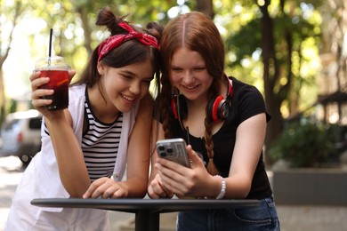 Happy teenage friends looking at smartphone in outdoor cafe