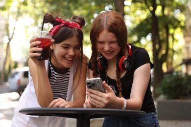 Happy teenage friends looking at smartphone in outdoor cafe