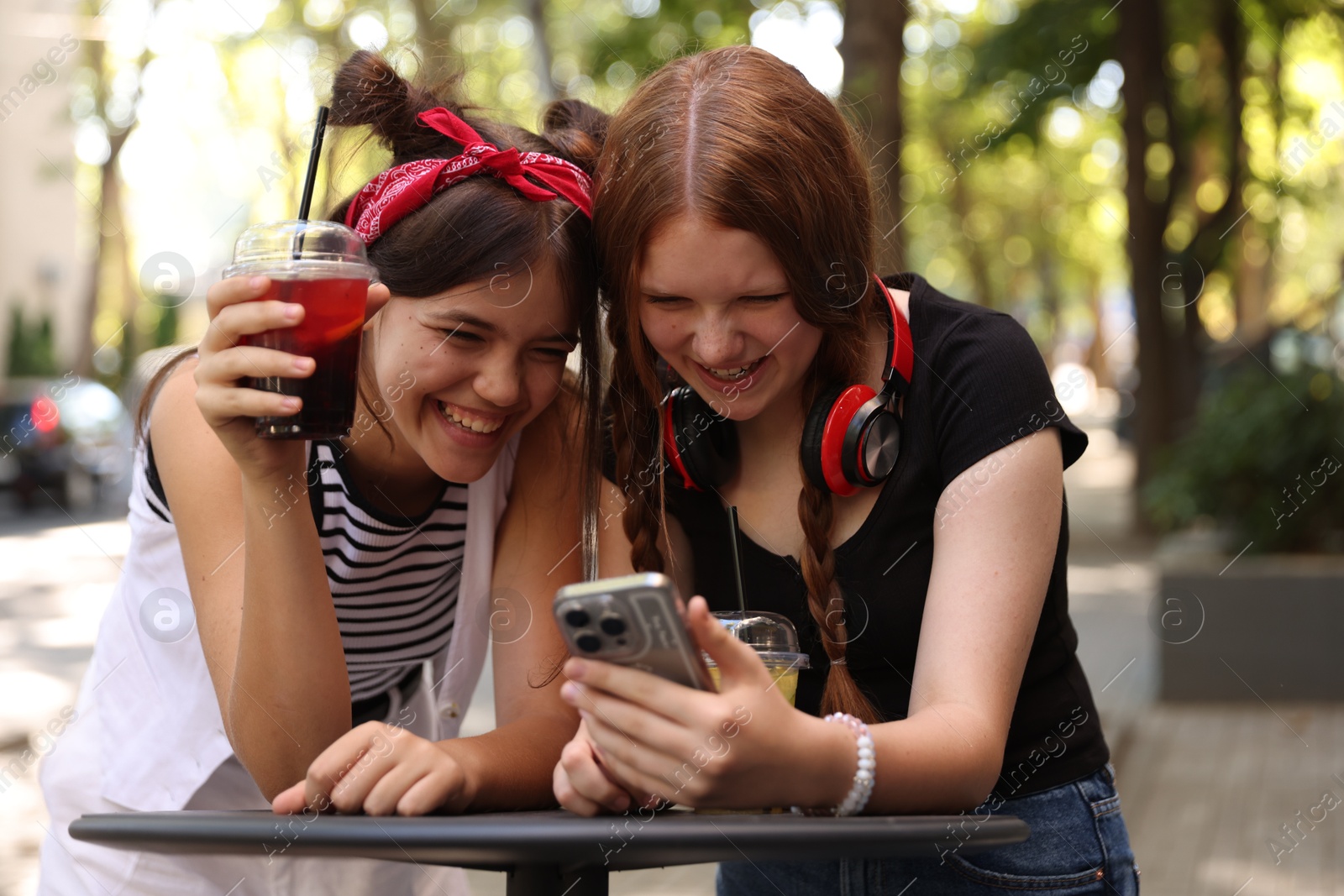 Photo of Happy teenage friends looking at smartphone in outdoor cafe