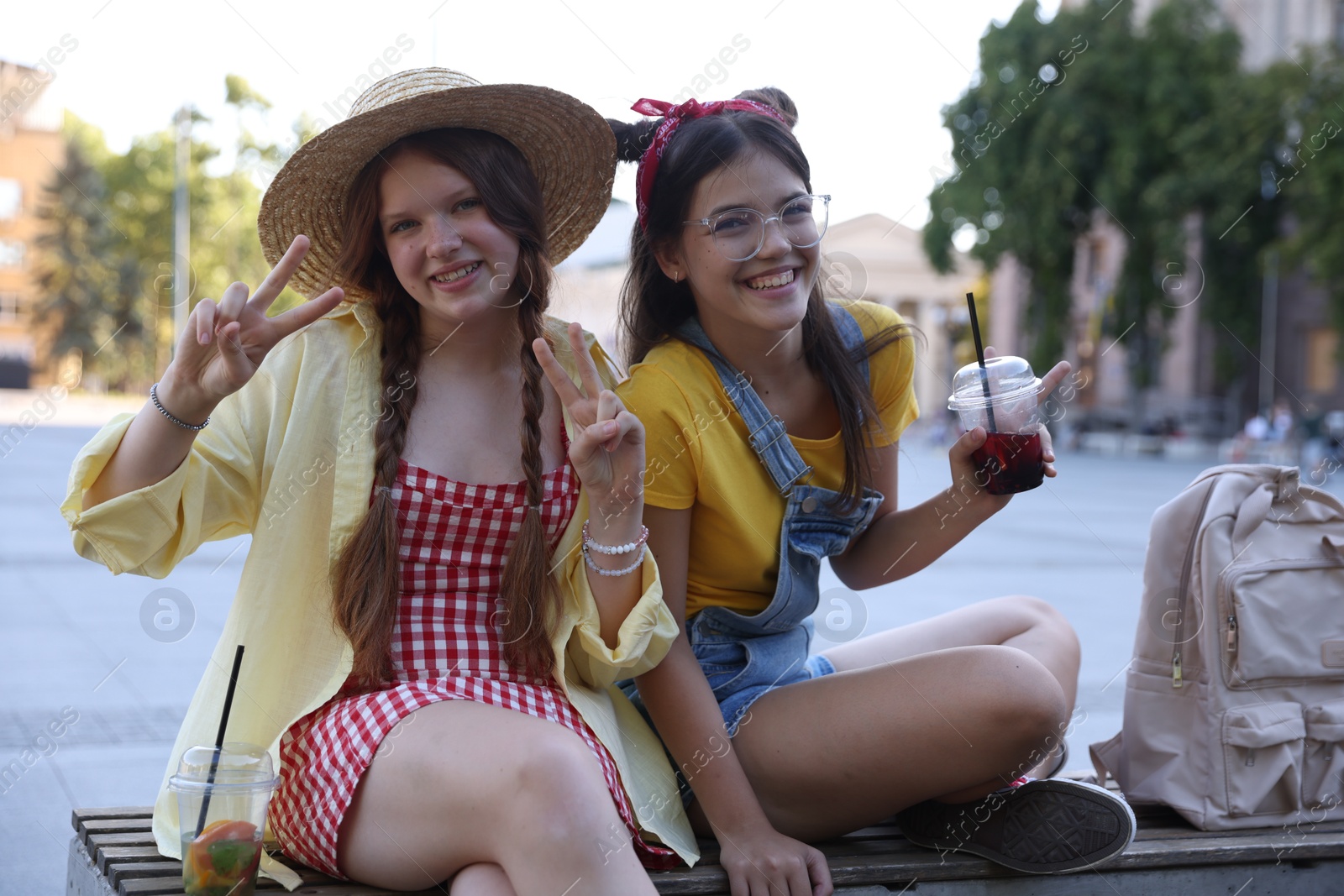 Photo of Happy teenage friends showing peace signs on bench outdoors