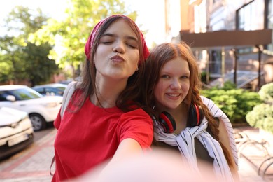 Happy teenage friends taking selfie on city street