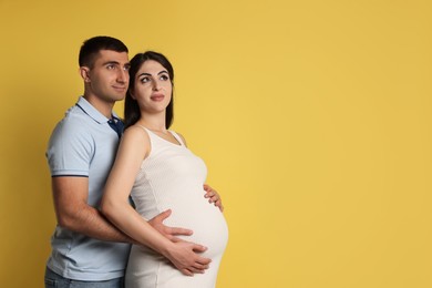 Photo of Beautiful pregnant woman with her husband on yellow background, space for text