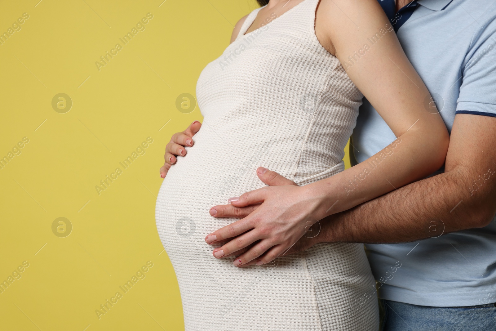 Photo of Man hugging her pregnant wife on yellow background, closeup. Space for text