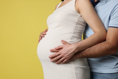 Photo of Man hugging her pregnant wife on yellow background, closeup. Space for text