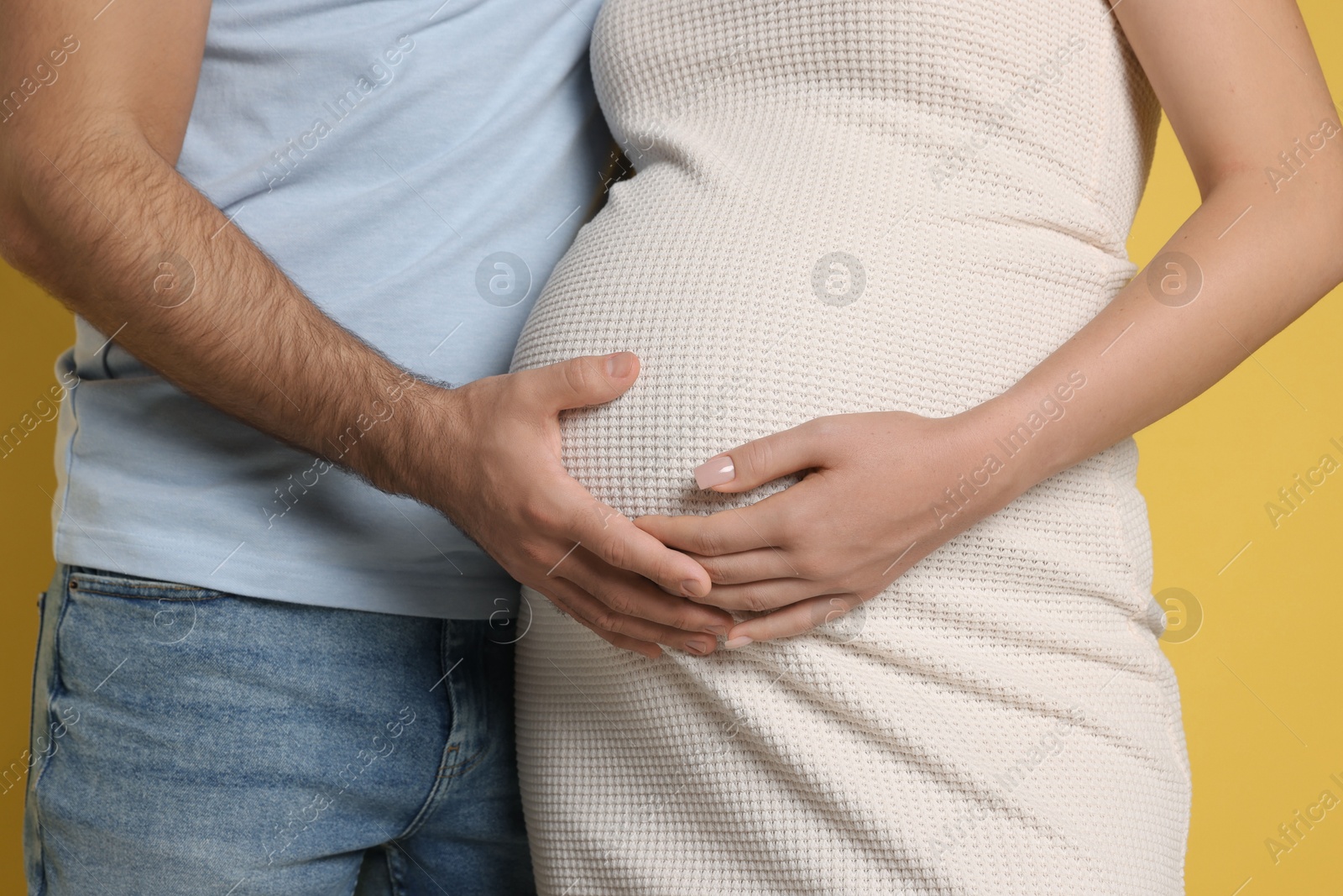 Photo of Pregnant woman with her husband touching belly on yellow background, closeup