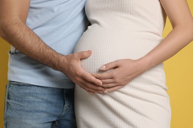 Photo of Pregnant woman with her husband touching belly on yellow background, closeup