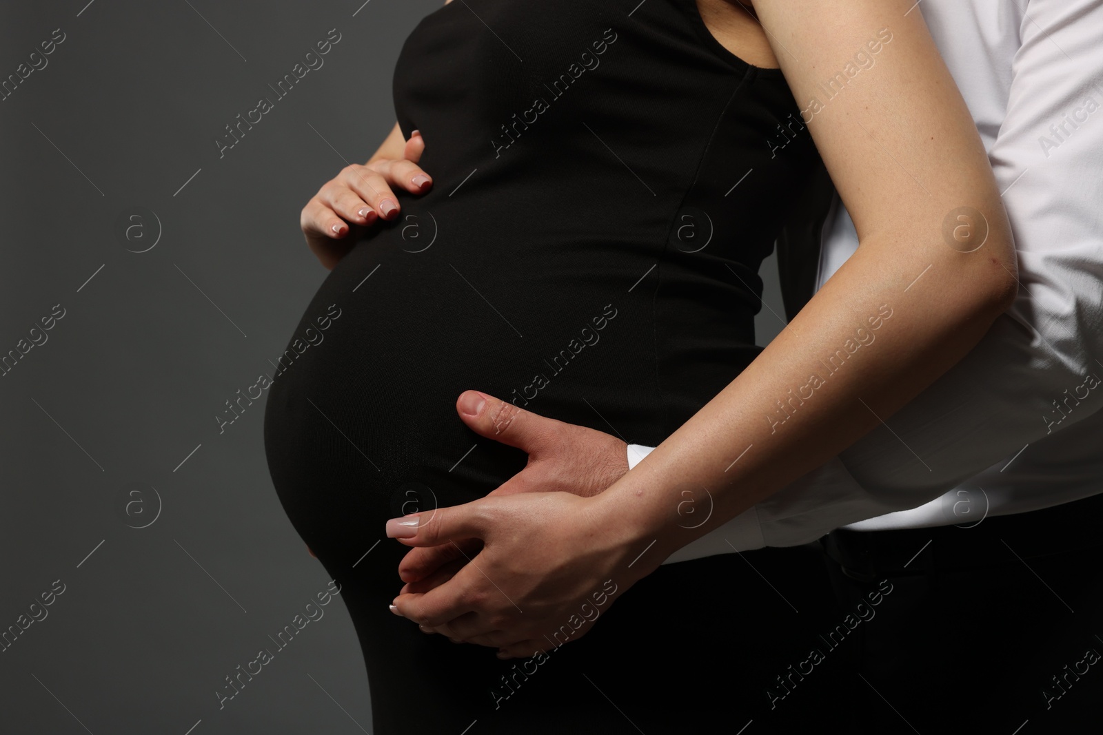 Photo of Pregnant woman with her husband touching belly on grey background, closeup