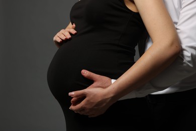 Photo of Pregnant woman with her husband touching belly on grey background, closeup