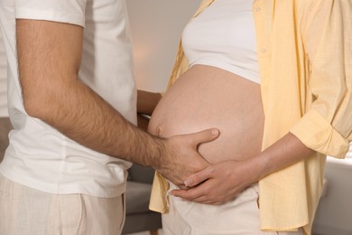 Photo of Man touching his pregnant wife's belly indoors, closeup