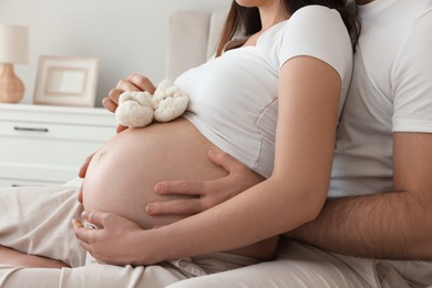 Photo of Pregnant woman with baby booties and her husband indoors, closeup