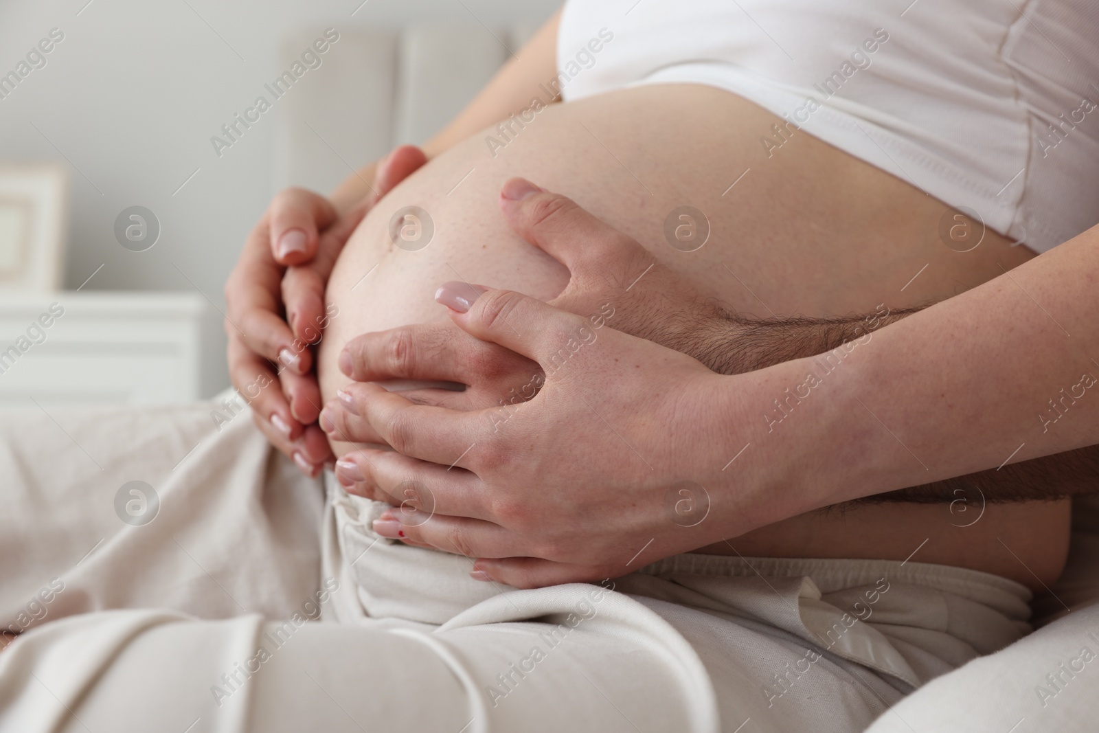 Photo of Man touching his pregnant wife's belly indoors, closeup