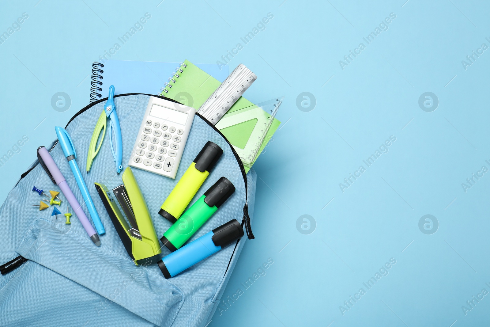 Photo of Backpack with different school stationery on light blue background, top view. Space for text