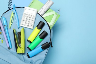 Photo of Backpack with different school stationery on light blue background, top view. Space for text