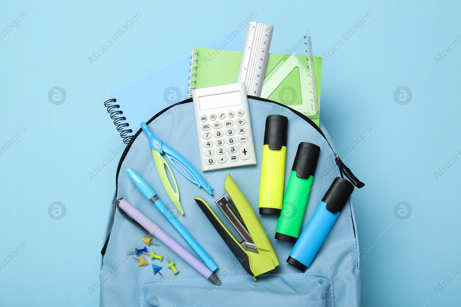 Photo of Backpack with different school stationery on light blue background, top view