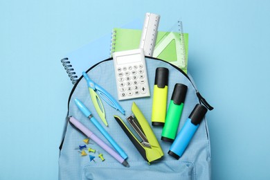 Photo of Backpack with different school stationery on light blue background, top view