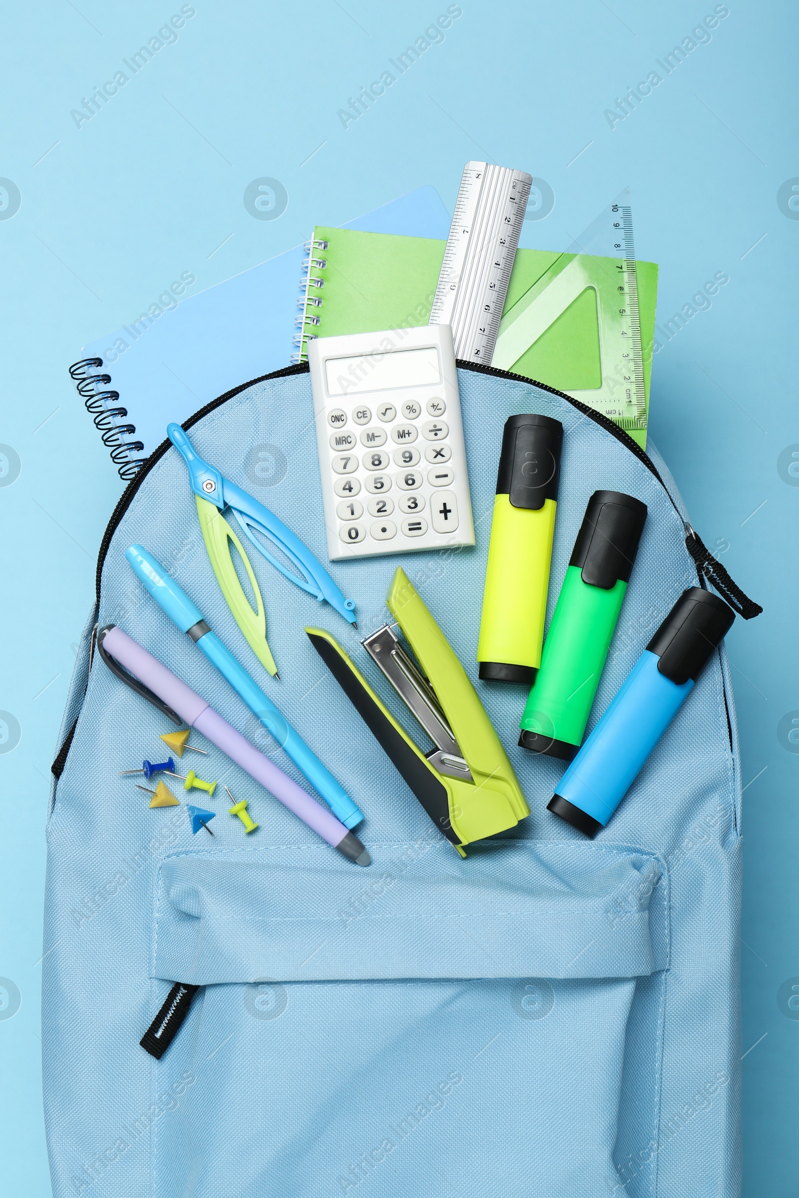 Photo of Backpack with different school stationery on light blue background, top view