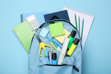 Photo of Backpack with different school stationery on light blue background, top view