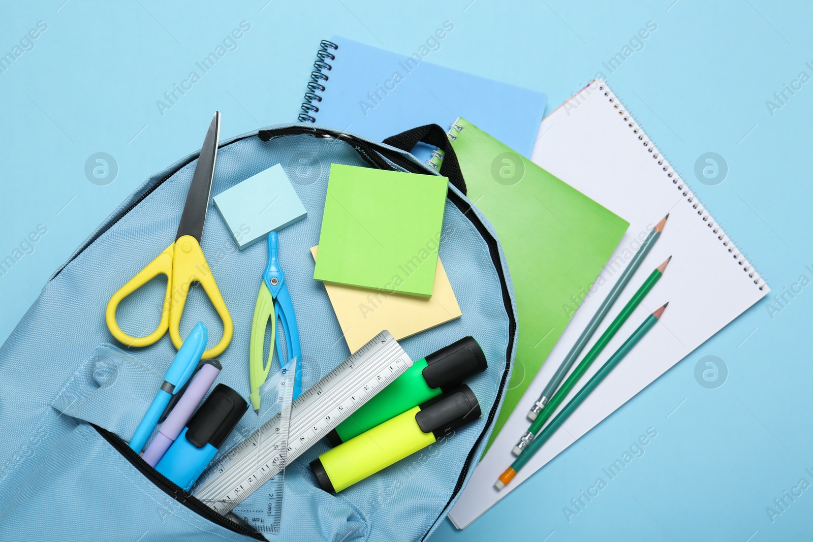 Photo of Backpack with different school stationery on light blue background, top view