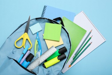 Backpack with different school stationery on light blue background, top view