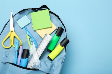 Backpack with different school stationery on light blue background, top view. Space for text