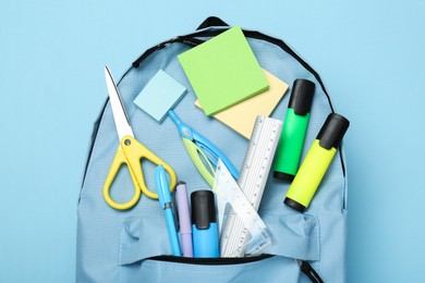 Photo of Backpack with different school stationery on light blue background, top view