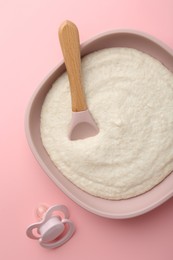 Photo of Delicious baby food in bowl, spoon and pacifier on pink background, top view