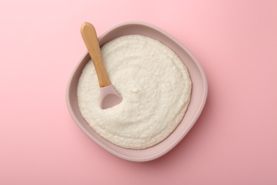 Photo of Delicious baby food in bowl and spoon on pink background, top view