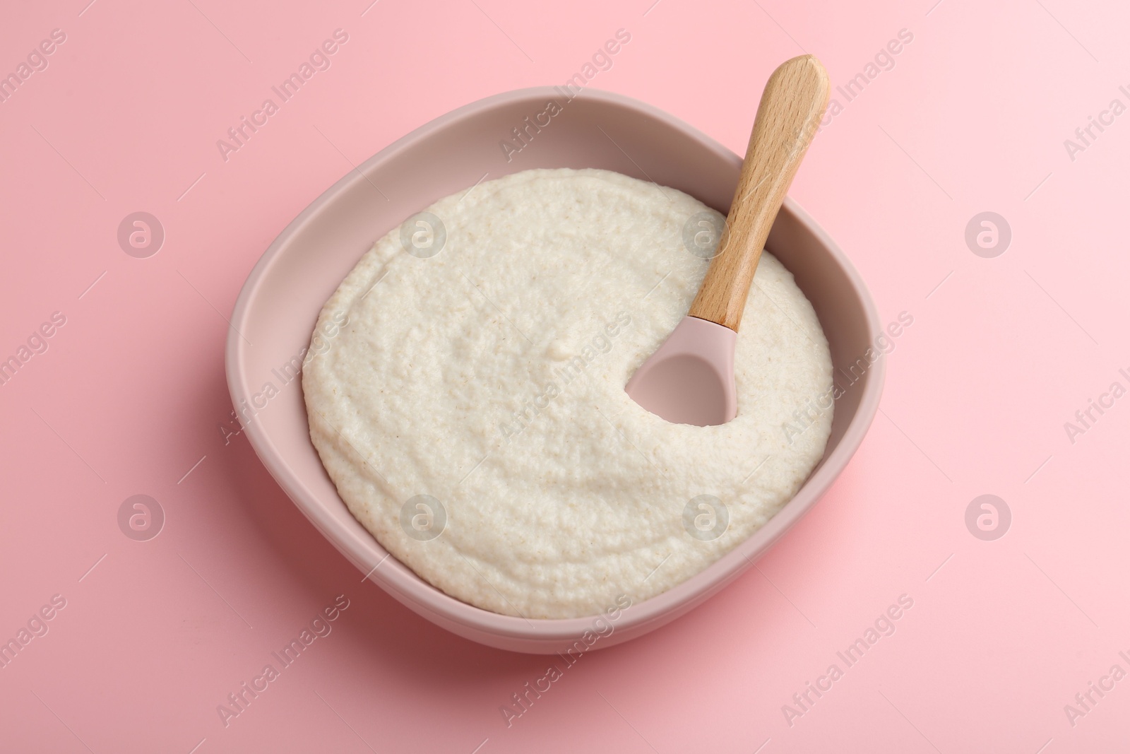 Photo of Delicious baby food in bowl and spoon on pink background