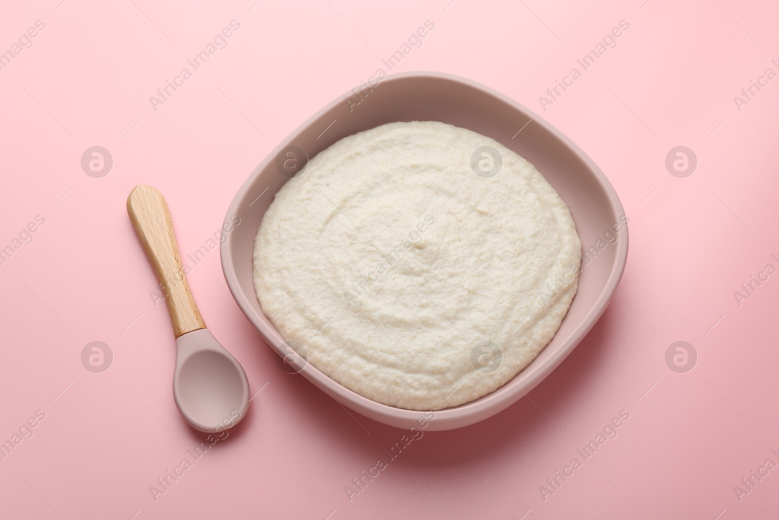 Photo of Delicious baby food in bowl and spoon on pink background